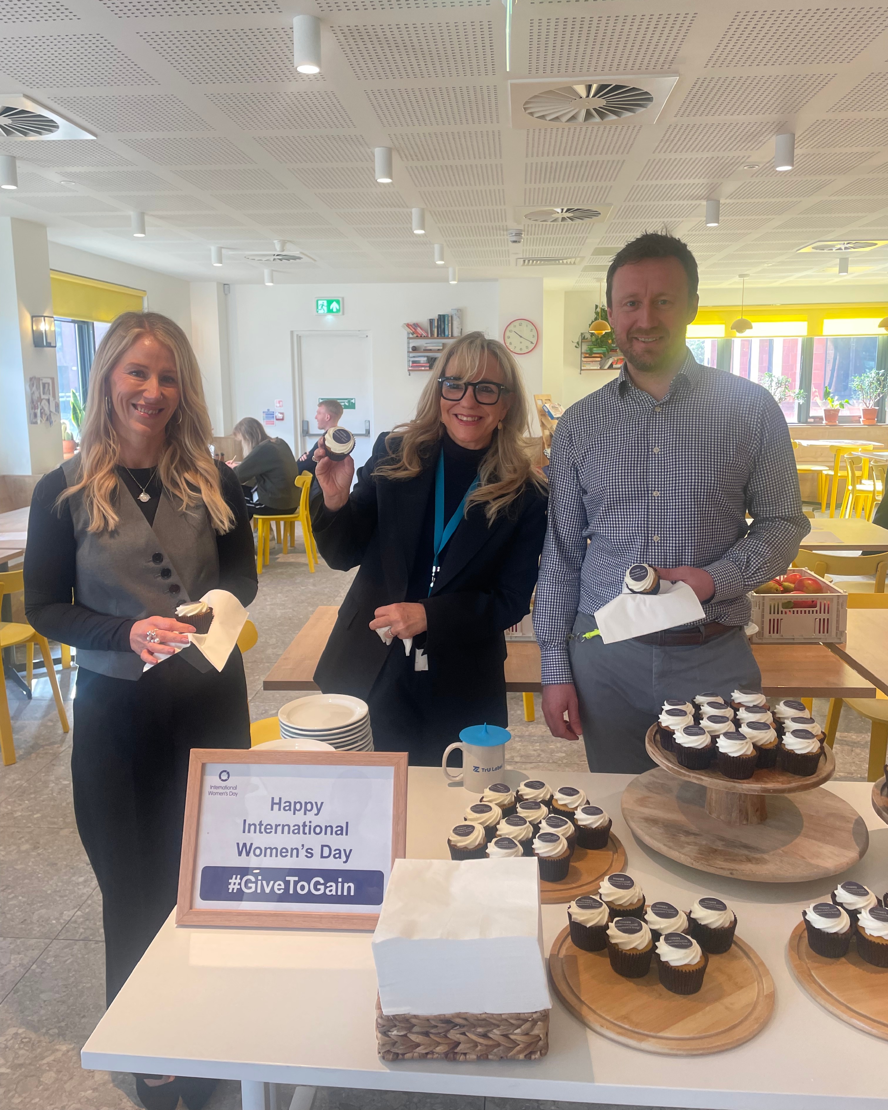 Two women and a man standing behind a table of cupcakes