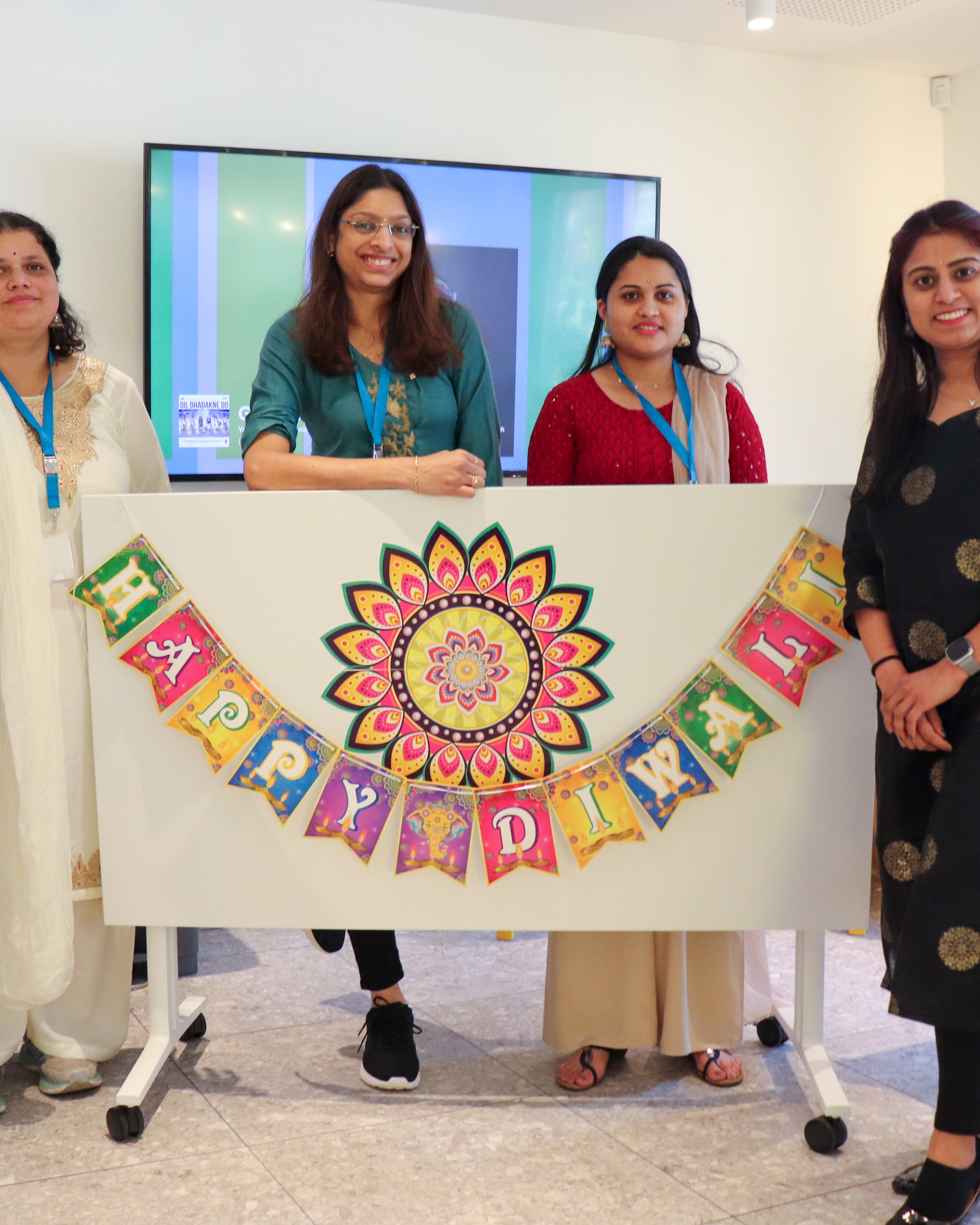 Four women in traditional Indian dress with a sign saying Happy Diwali between them